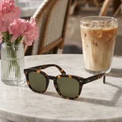 AI product photo: tortoiseshell sunglasses on a marble café table beside pink flowers and an iced coffee